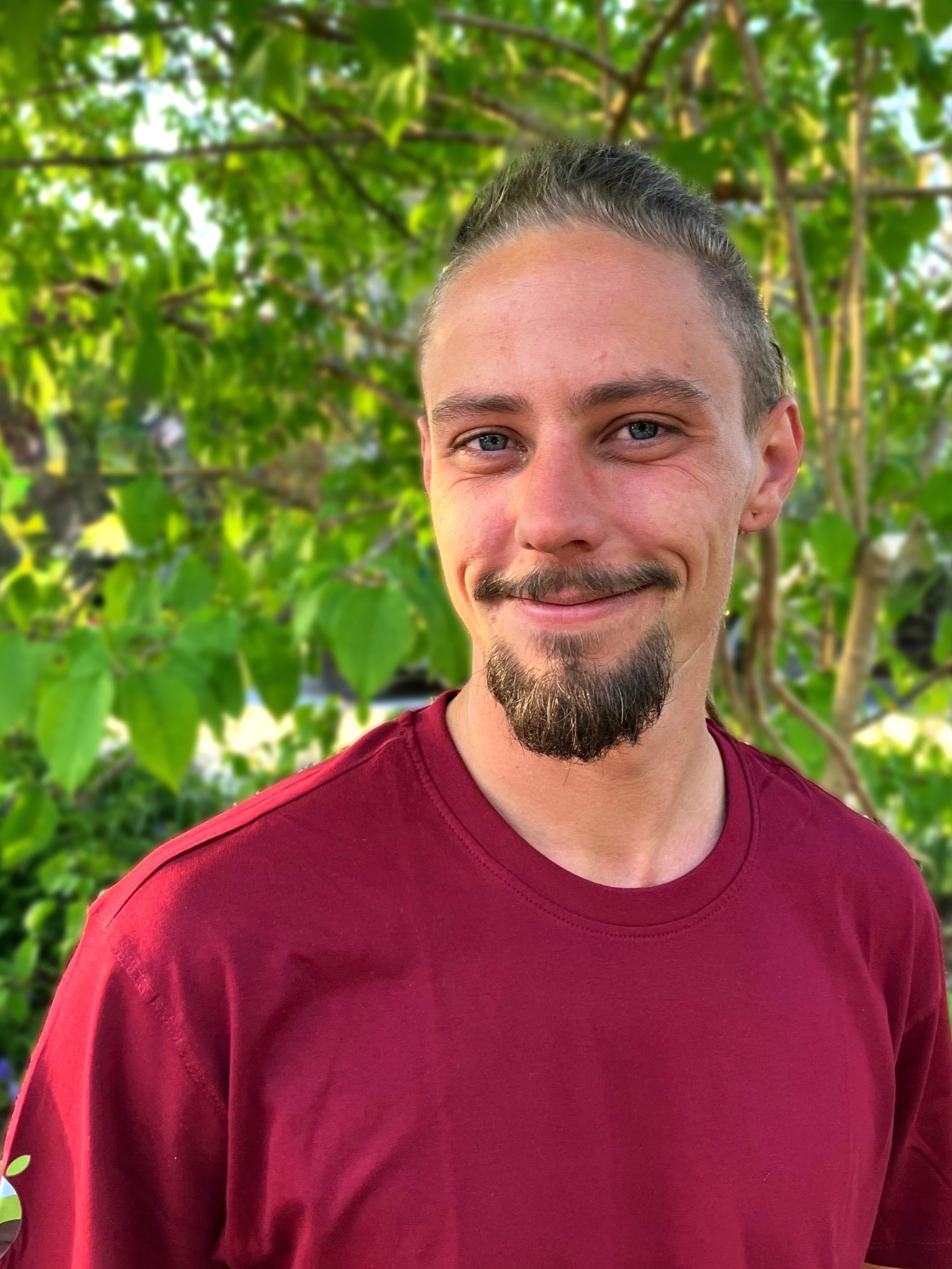 Mann mit kurzem, dunklem Haar und rotem T-Shirt, der in die Kamera lächelt.
