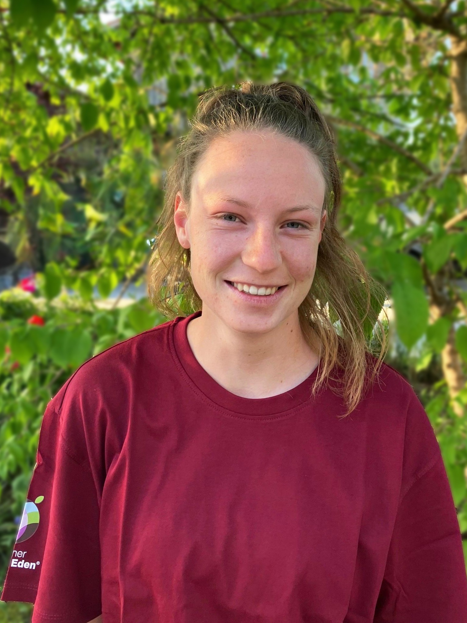 Junge Frau mit kurzen blonden Haaren und rotem T-Shirt lächelt in die Kamera.
